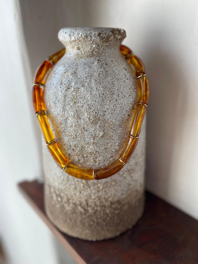 Colar Resina em tons âmbar pendurado numa jarra de cerâmica moderna e rústica.