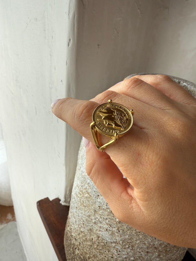 Anel robusto e elegante com moeda, ajustando-se perfeitamente ao dedo com acabamento dourado.