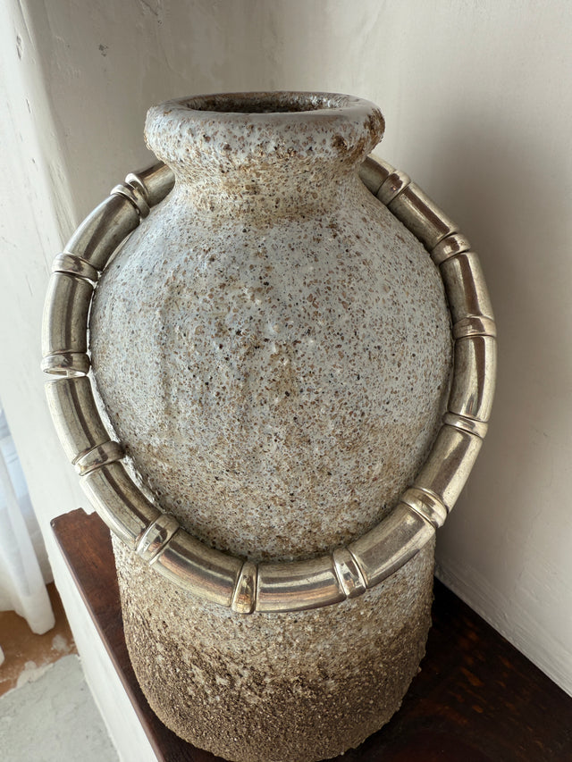 Colar metálico elegante adornando vaso de cerâmica, perfeito para decoração sofisticada e contemporânea.