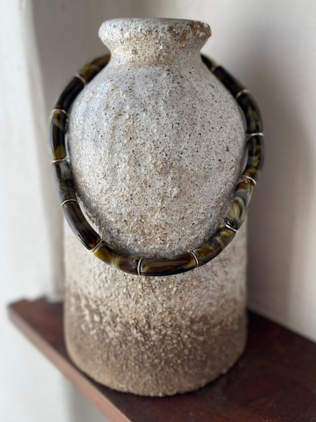 Colar Resina elegante em tons modernos, pendurado em vaso de cerâmica rústica.