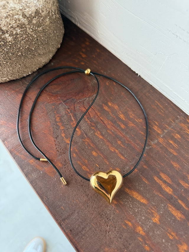Colar Corda Coração Ajustável com coração dourado e fio de corda preta, ideal para looks casuais e sofisticados.
