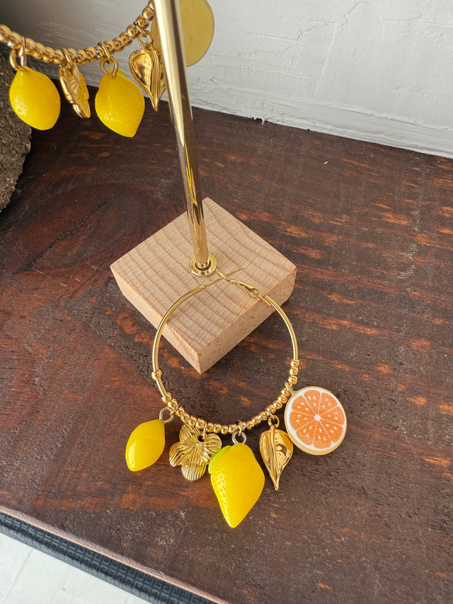 Argolas douradas com pendentes de limão e laranja, acessórios vibrantes inspirados no verão mediterrânico.