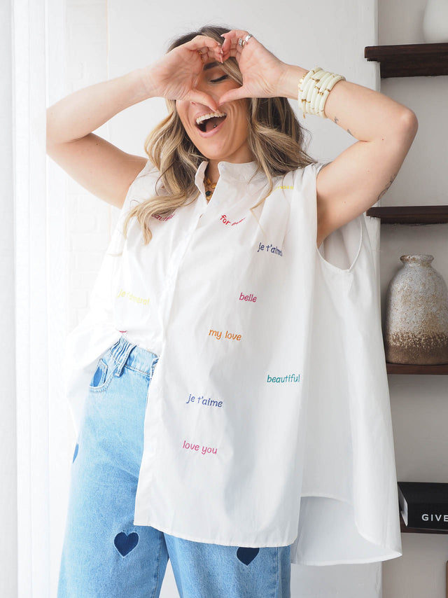 Model wearing oversized white blouse with embroidered colorful words, expressing joy and style in a chic setting.