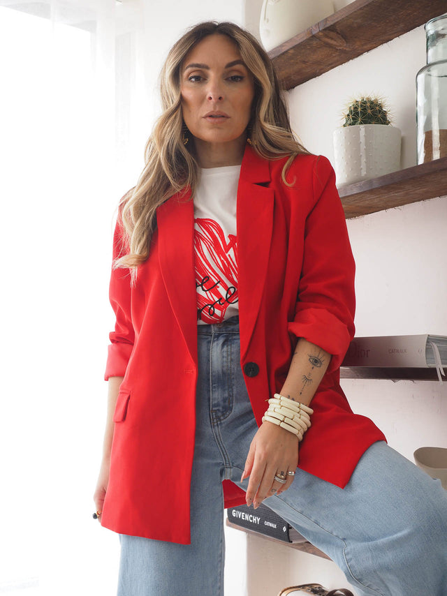 Modelo com blazer vermelho de corte reto, camiseta estilosa e jeans, exibindo um look moderno e sofisticado.