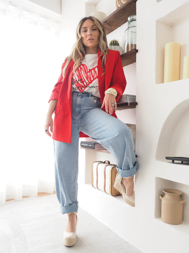 Woman wearing a red basic blazer with a graphic tee and rolled-up jeans, styled in a modern indoor setting.
