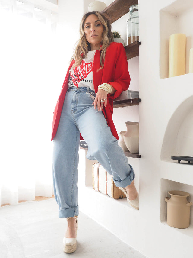 Modelo usando calças de ganga wide balloon com uma blusa estilosa e blazer vermelho em ambiente moderno.