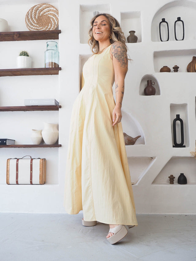 Modelo usando um vestido comprido de alças amarelo, destacando elegância e estilo em ambiente moderno.