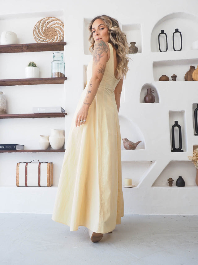 Modelo usando vestido comprido de alças amarelo, elegante e sofisticado, em ambiente minimalista.