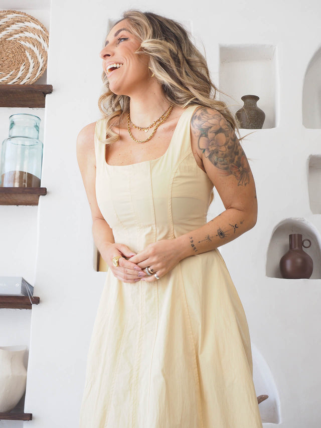 Mulher sorrindo usando vestido comprido de alças amarelo, destacando elegância e estilo.