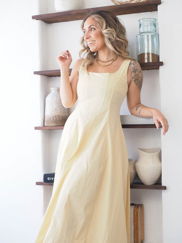 Modelo sorrindo usando vestido comprido de alças amarelo, exibindo elegância e sofisticação.
