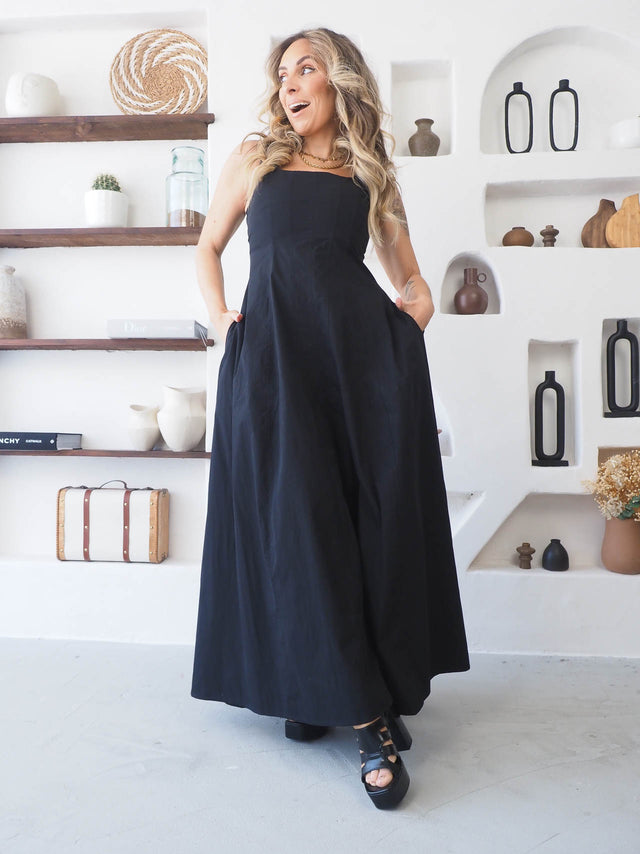 Modelo usando vestido comprido de alças preto, elegante e sofisticado, em ambiente moderno e minimalista.