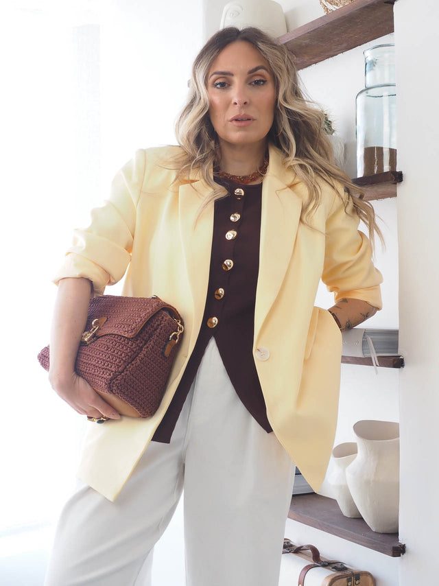 Mulher com blazer básico corte reto amarelo segurando bolsa, exibindo estilo moderno e sofisticado.