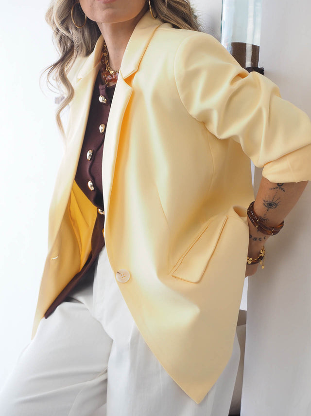 Mulher usando um blazer básico de corte reto amarelo com gola em lapela e bolsos, estilo moderno e sofisticado.