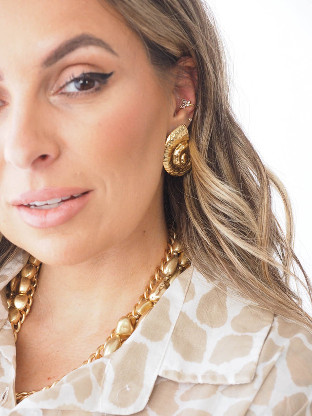 Mulher sorridente usando brincos earcuff dourados e colar, estilo elegante e descontraído.