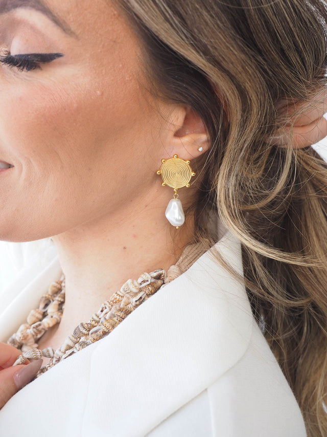 Brincos circulares dourados com pedra branca, elegantes e sofisticados, usados em look casual.