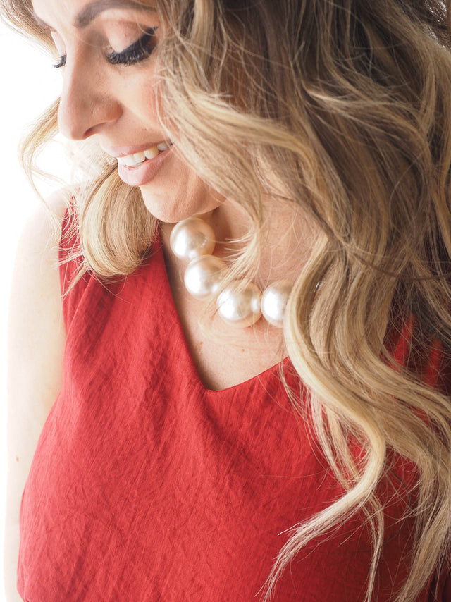 Colar de pérolas grandes, elegante e sofisticado, complementando um vestido vermelho, ideal para ocasiões especiais.