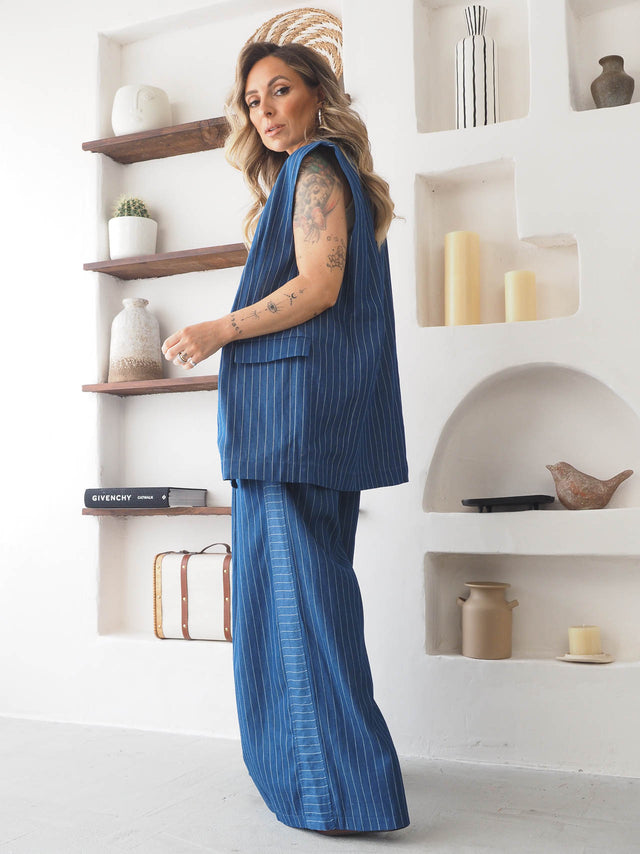Modelo elegante em calças pantalona às riscas, de cintura alta e corte largo, destacando conforto e sofisticação.