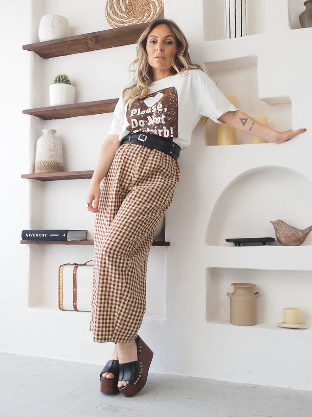 Mulher com calças xadrez largas e t-shirt estilosa, mostrando conforto e moda versátil em ambiente moderno.
