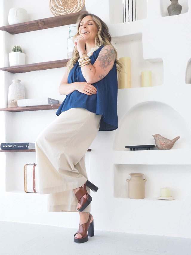 Mulher sorridente em calças largas e blusa azul, mostrando estilo e conforto em ambiente moderno.