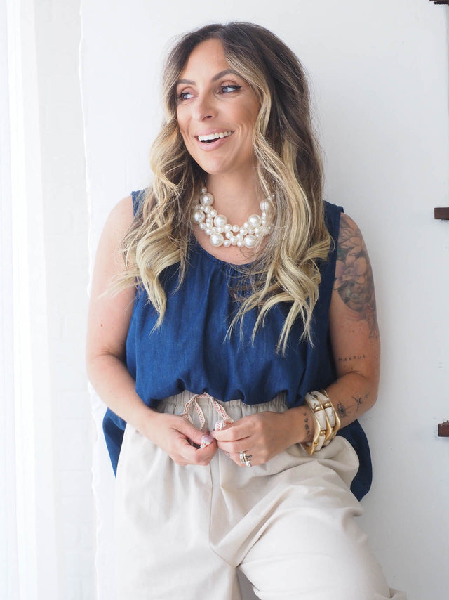 Mulher sorridente com blusa de ganga azul e acessórios modernos, transmitindo estilo e conforto.