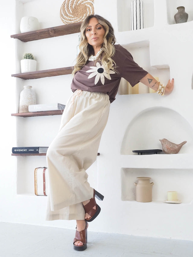 Mulher com t-shirt flor bordada em look casual e elegante, usando calças largas e sandálias.