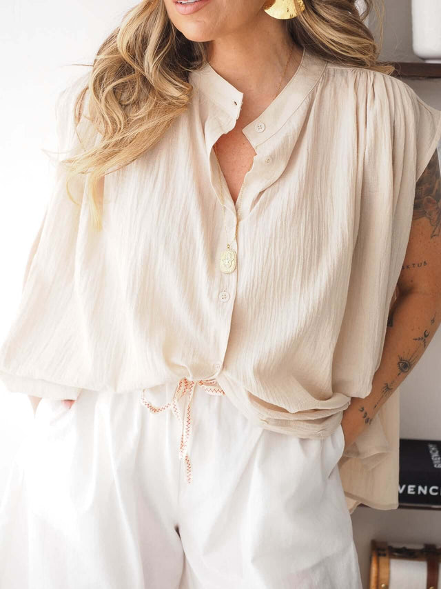 Camisa Manga Cava oversized em tom neutro, com fecho de botões, gola redonda e corte solto, feita em malha leve.