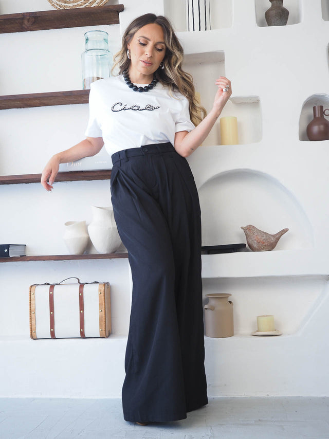 Mulher com calças com pregas de cintura alta e t-shirt, num ambiente elegante e moderno.