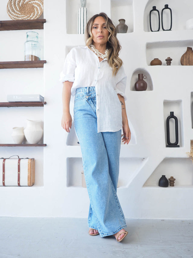 Modelo usando jeans wide leg cintura cruzada com camisa branca, destacando estilo e conforto.