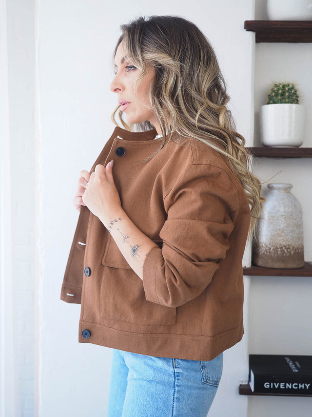 Mulher de perfil a usar um blusão curto castanho com botões, combinando com jeans. Elegância e estilo intemporal.