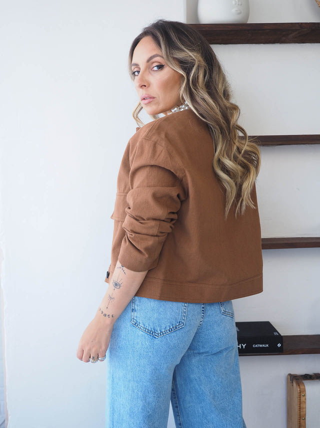 Mulher com blusão curto castanho, de costas, combinando com jeans azuis, look casual-chic.