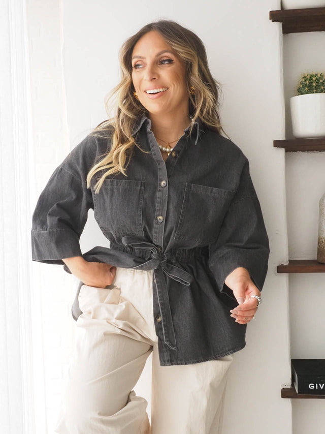 Camisa de ganga ajustável em cinza, com cinto, combinada com calças largas para um look casual e elegante.