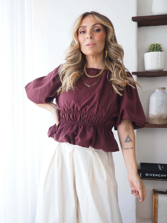 Blusa bordô de mangas balão e cintura elástica, mão na cintura, vista de frente.