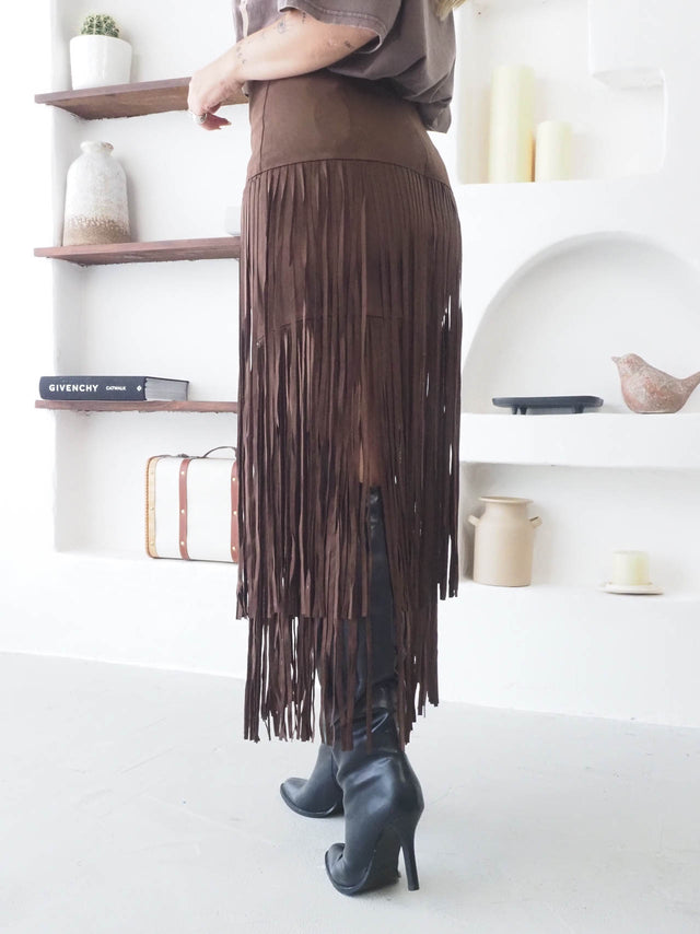 Saia com franjas em camurça castanho, ideal para looks boho-chic e modernos, combinada com botas de salto.