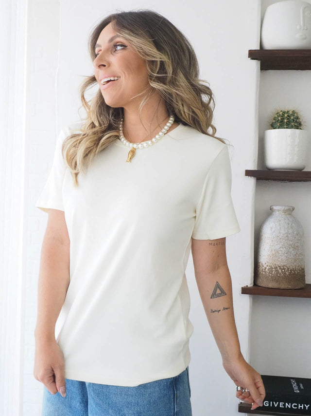 t-shirt básica de manga curta em tom claro, ideal para looks casuais e elegantes, combinada com colar de pérolas.