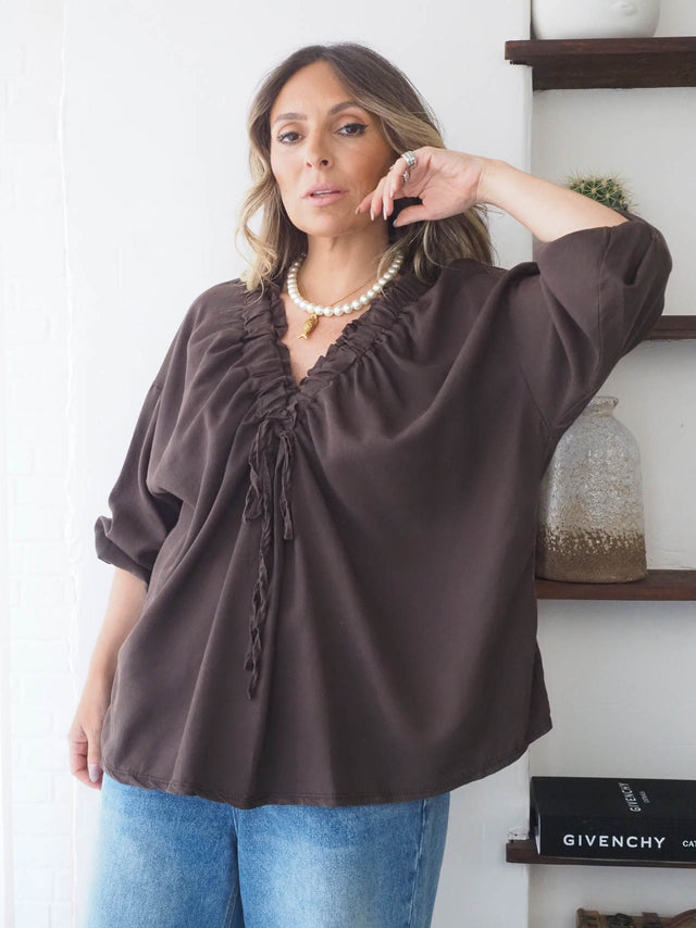 Blusa com drapeado frontal em tom castanho, manga larga, ideal para looks versáteis e elegantes, combinada com jeans.