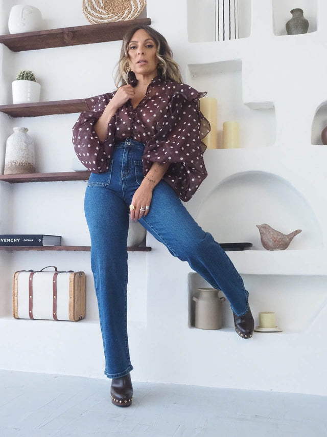 Mulher a usar Calças de Ganga Regular Bootcut em ambiente moderno, com blusa de bolinhas e pormenores de design.