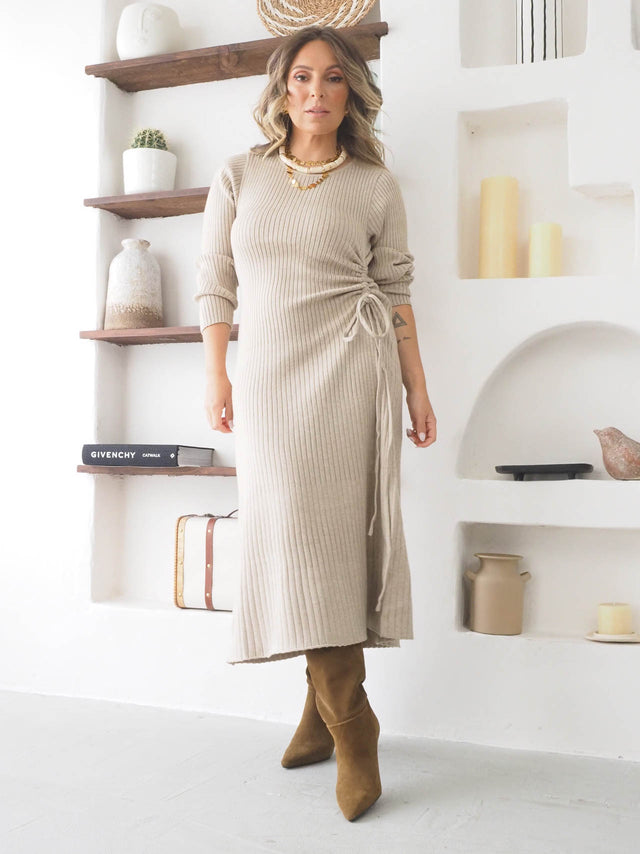 Modelo usando vestido de malha comprido em tom neutro, com detalhes em cordão e botas elegantes.