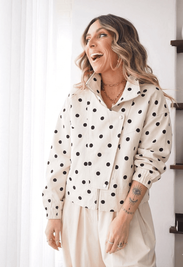 Mulher sorridente a usar um Blusão de Ganga às Bolas com padrão de bolinhas, ideal para looks modernos e sofisticados.