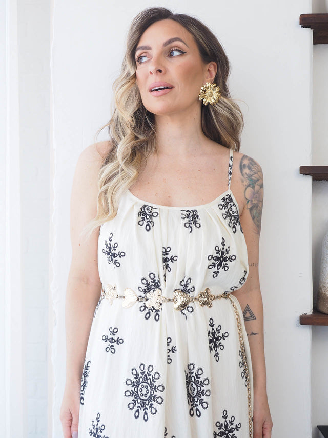 Mulher elegante usando vestido branco com detalhes em preto e brincos florais, mostrando estilo e sofisticação.