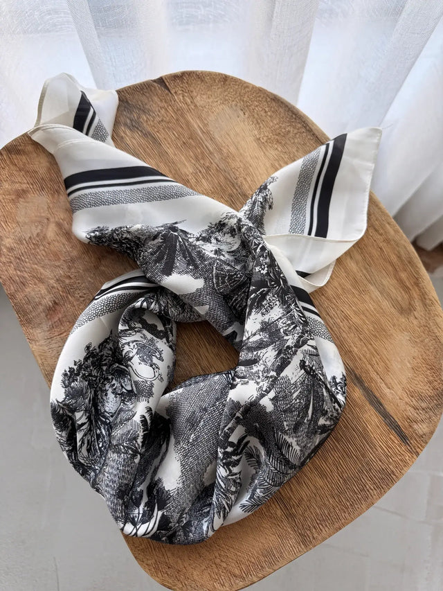 Lenço Quadrado Estampado em tons de preto e branco sobre mesa de madeira.