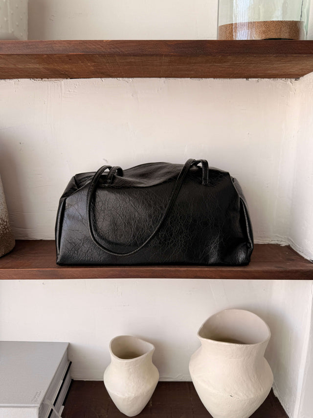 Tote Bag Ecopele em preto, com alças, sobre prateleira de madeira.