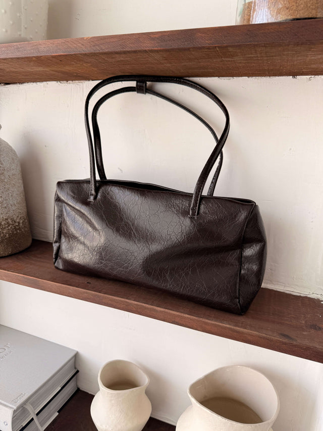 Tote Bag Ecopele em material castanho sobre prateleira de madeira