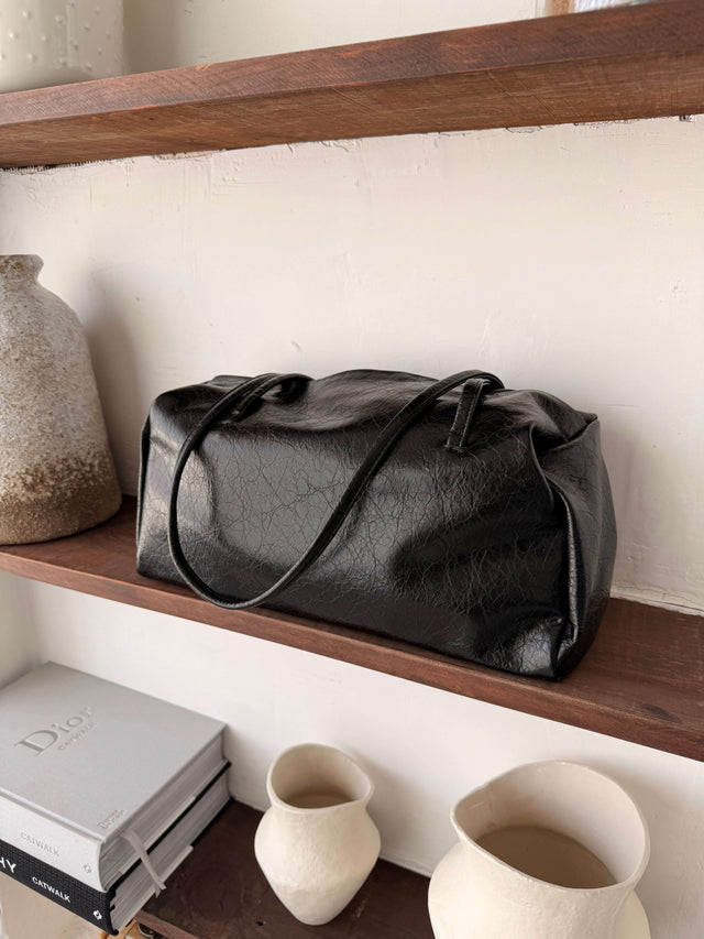 Tote Bag Ecopele preta em textura suave, sobre prateleira de madeira.