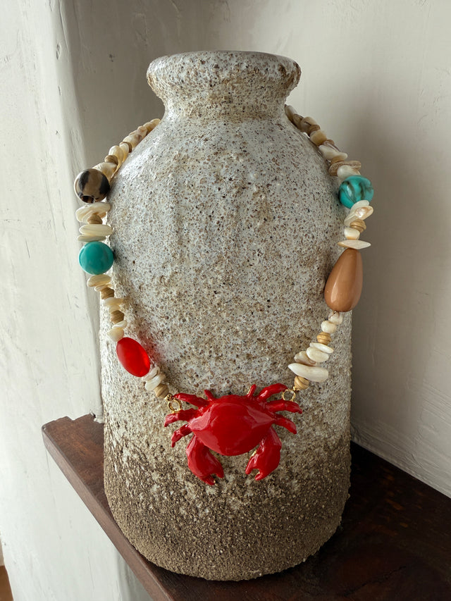 Colar Caranguejo Vermelho com pedras coloridas, estilo marinho, exibido em um vaso de cerâmica.