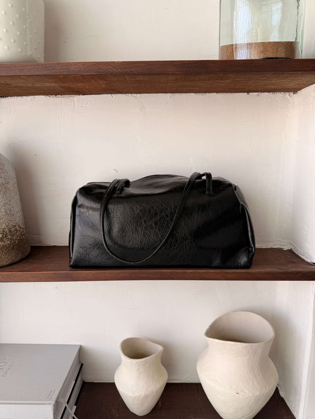 Tote Bag Ecopele preta em prateleira de madeira, exibindo design sofisticado.