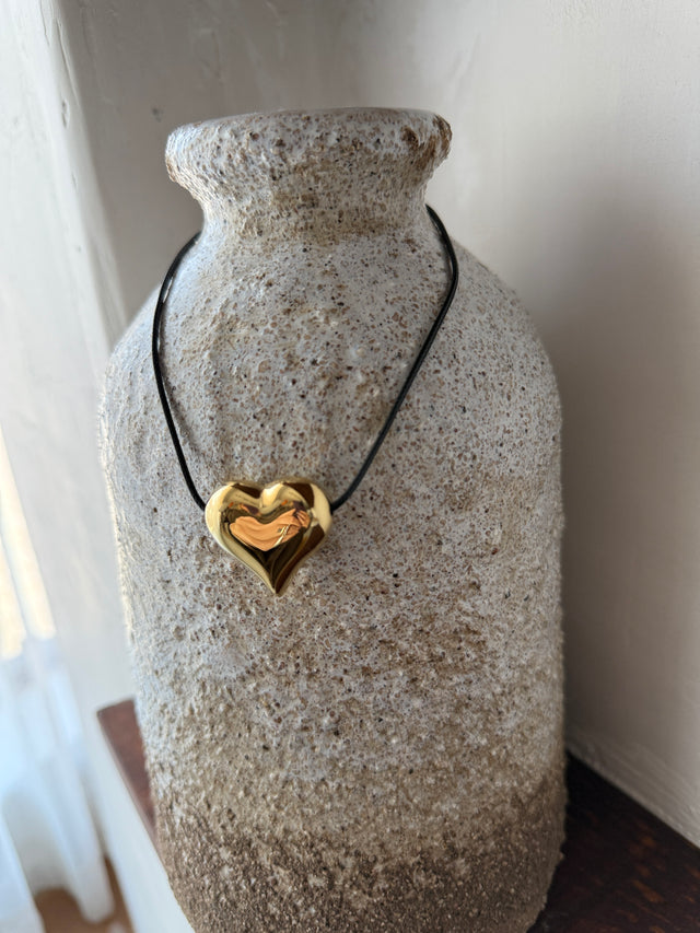 Colar ajustável com coração dourado em fio de corda preta, em vaso decorativo.