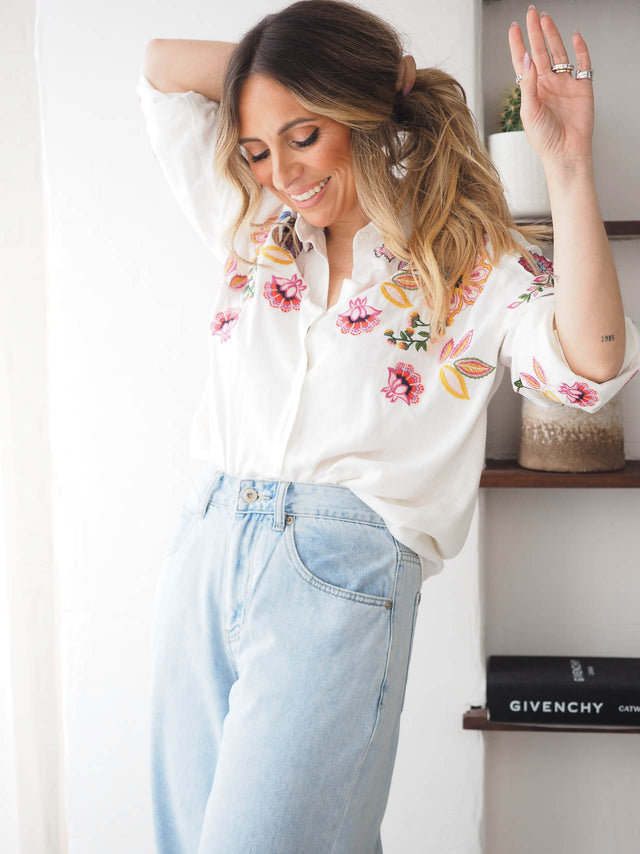 Vista frontal da camisa branca com fecho de botões e detalhes bordados.