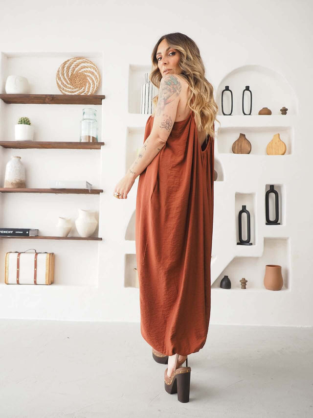 Mulher de costas usando um Macacão Largo de Alças laranja, com design fluido e elegante.