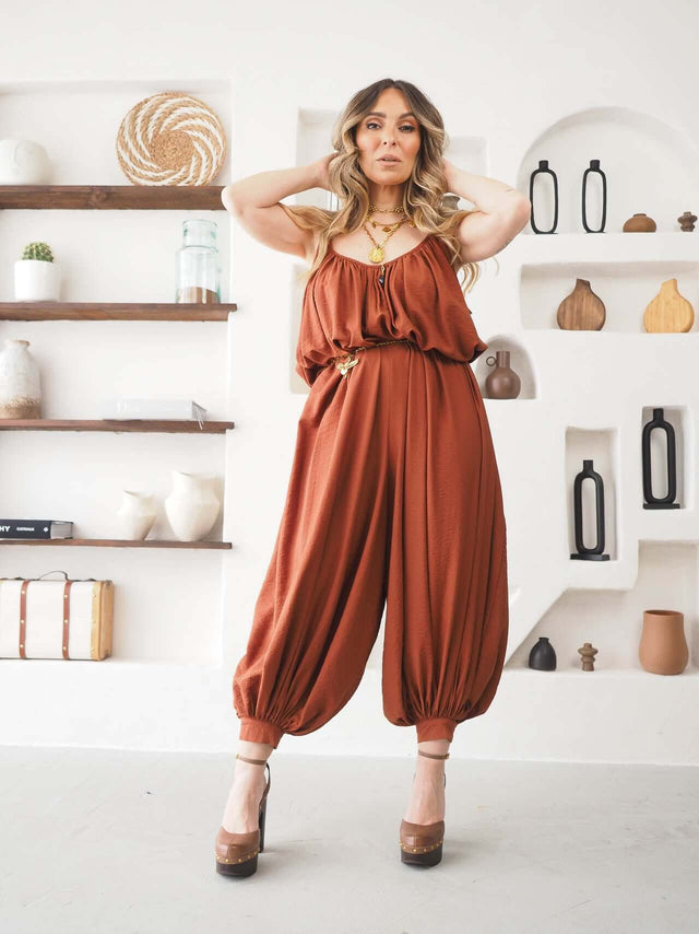Mulher vestindo um Macacão Largo de Alças em tom terracota, com design fluido e alças finas.