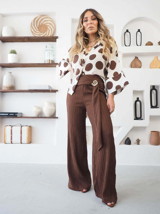 Camisa Bolas feminina com padrão polka dots, combinada com calças largas marrons, trazendo elegância e estilo moderno.